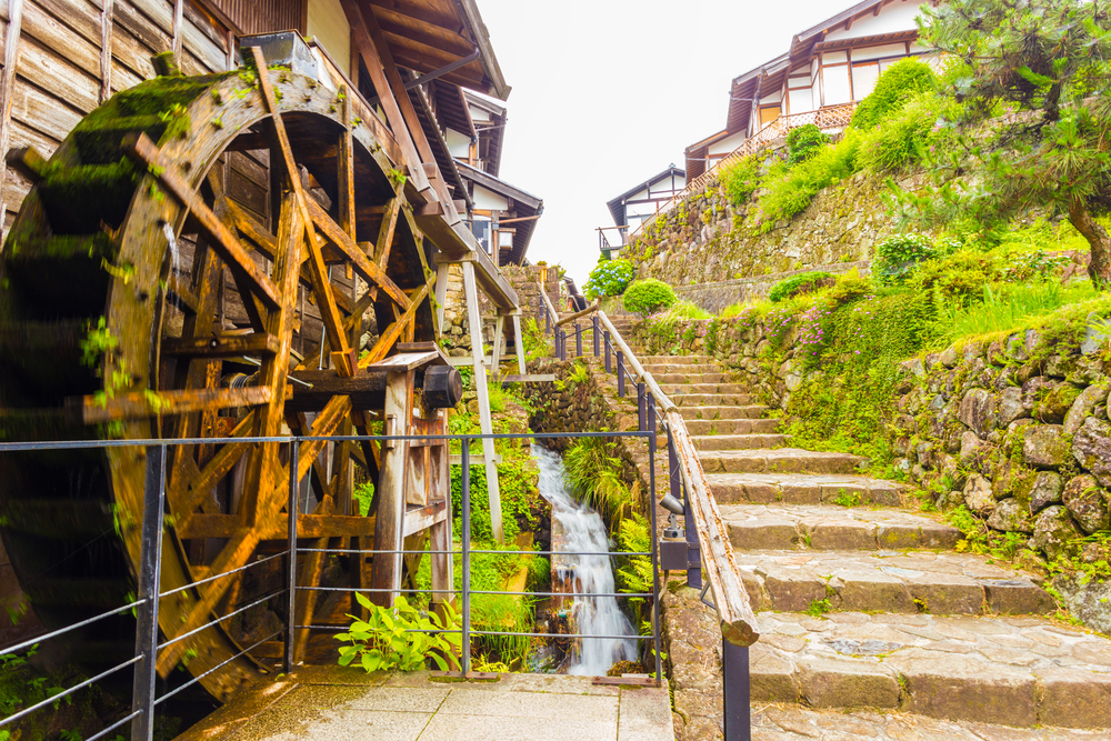 A small stream turns a motion blurred wooden water wheel next to beautifully restored stone steps on the historic Nakasendo trail in Magome, Kiso Valley.