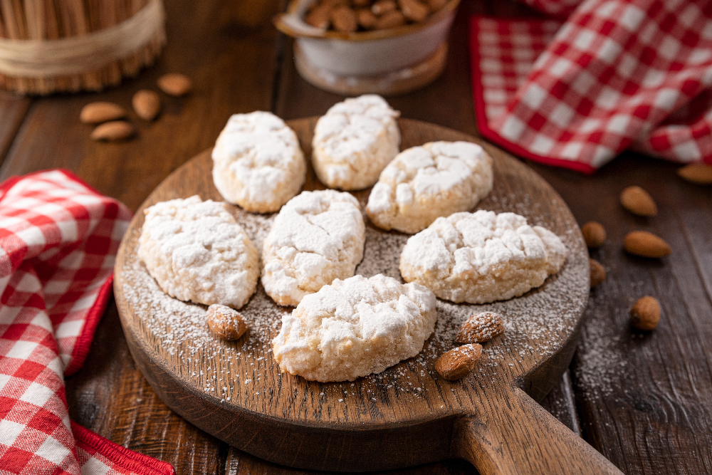 Sicilian almond cookies on a wooden board dusted with confectioners sugar on top.