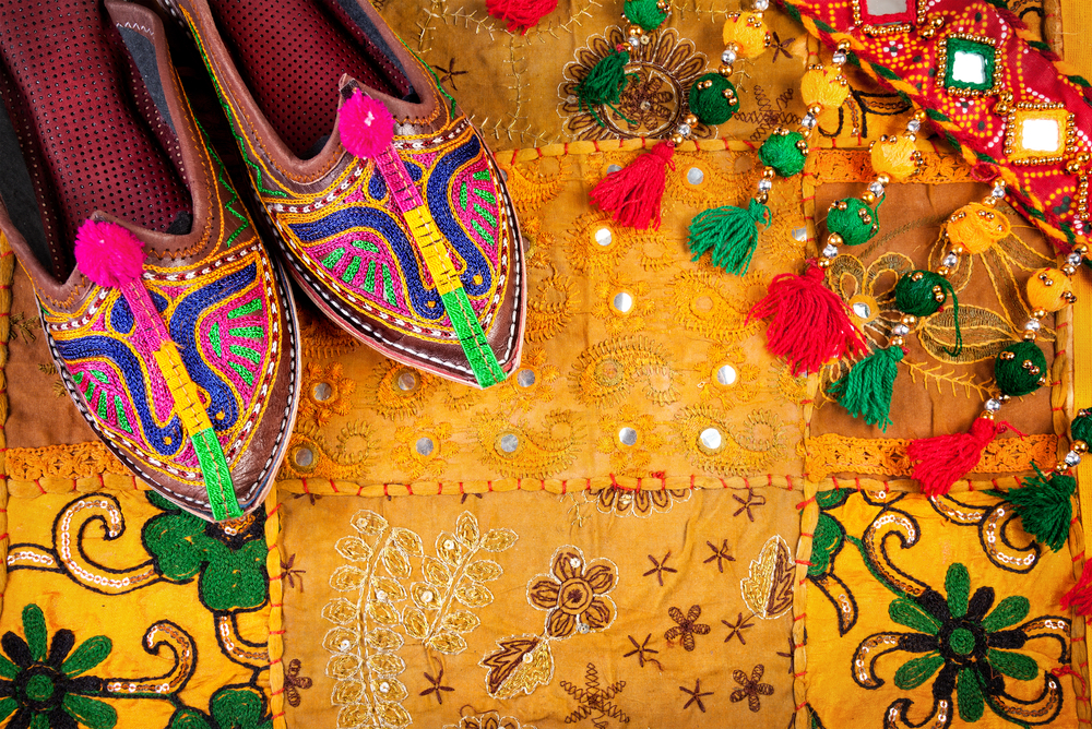 Colorful ethnic shoes and gipsy belt on yellow Rajasthan cushion cover on flea market in India.