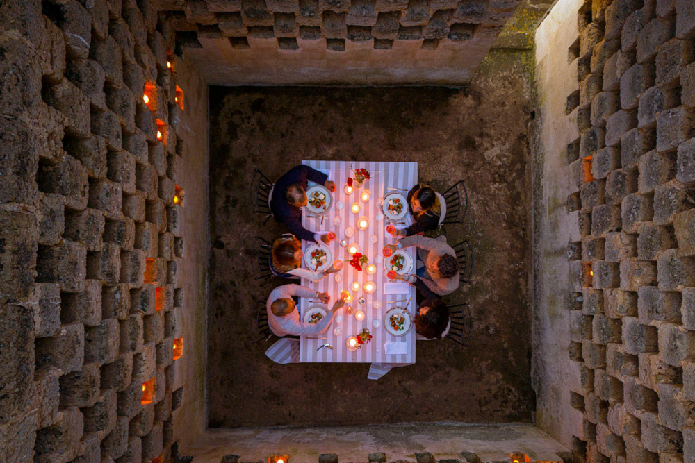 Over the top image of six people having a private dinner in an old Italian building with lots of candles and flowers.