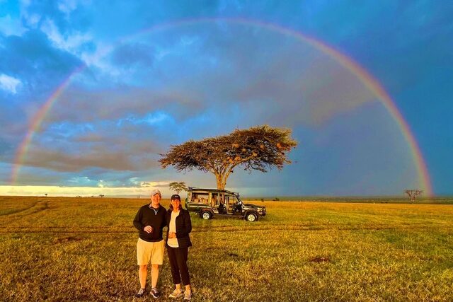 Travelers taking photo with the rainbow behind them at the safari in Masa Mara Conservancy, Kenya.