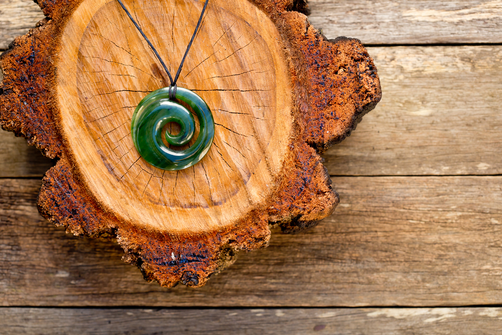 Maori green jade Koru pendant on wood log.