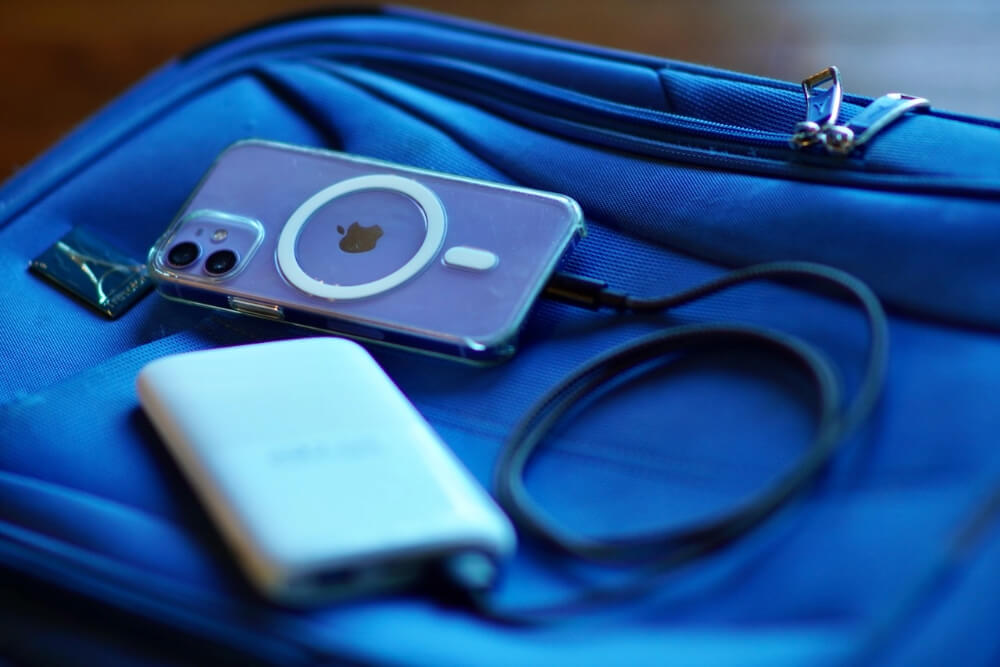 A cell phone charging with a power bank, on a blue suitcase.