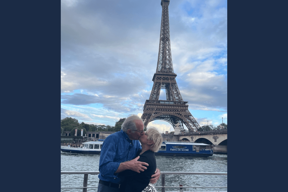 Sandy Collins and her husband kissing with river Seine and Eiffel tower in the background.