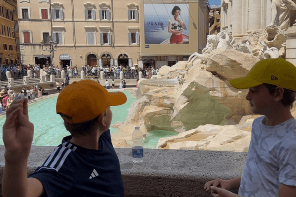 Two boys tossing coins at the Trevi Fountain in Rome.