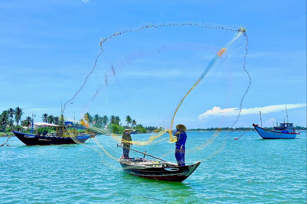 Fishermen casting a net from a boat in Vietnam.
