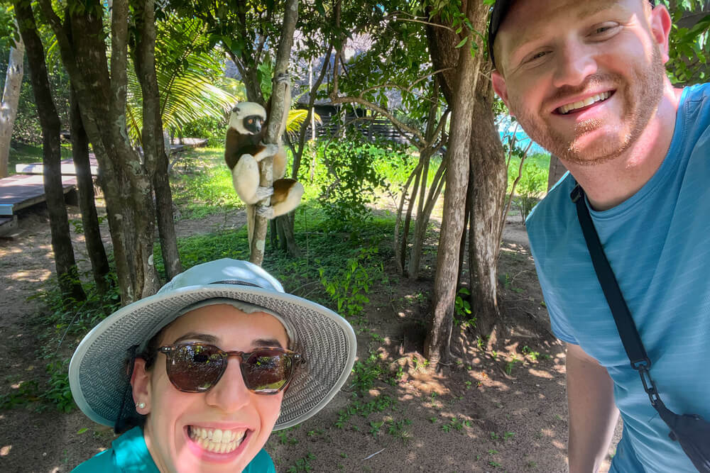 Rachel Zive and Sam Barnett posing with a Sifaka lemur on a rainforest hike in Anjajavy, Madagascar.