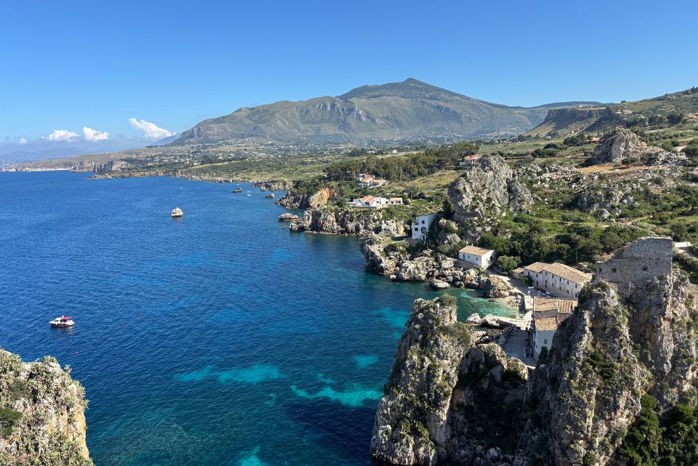 A sunny day, a blue beach, and limestone rocks in the village of Scopello, Sicily.