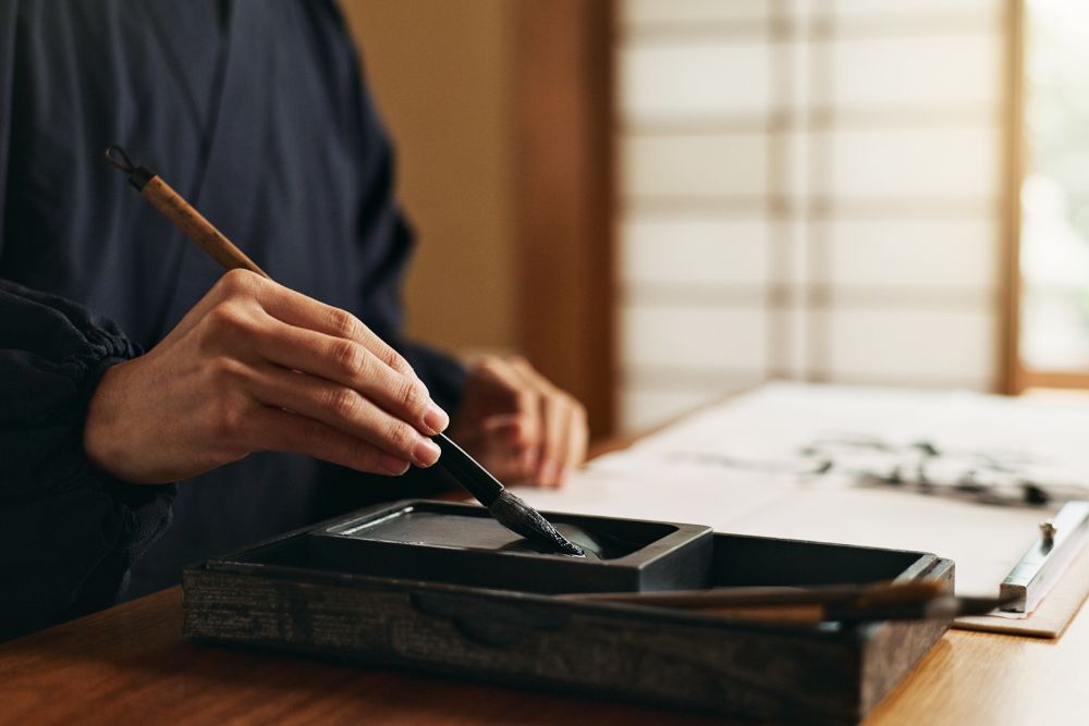 Close-up of hand writing Japanese calligraphy using traditional brush and ink.