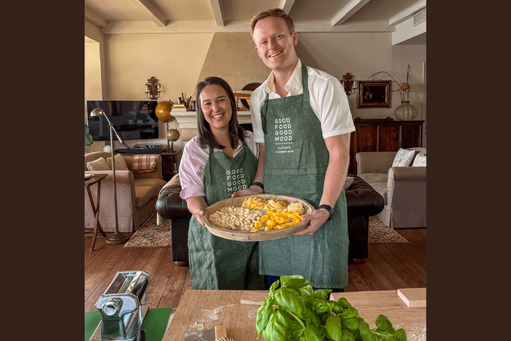 Marcus Conrad and his wife holding a plate of pasta during a cooking class in Italy.
