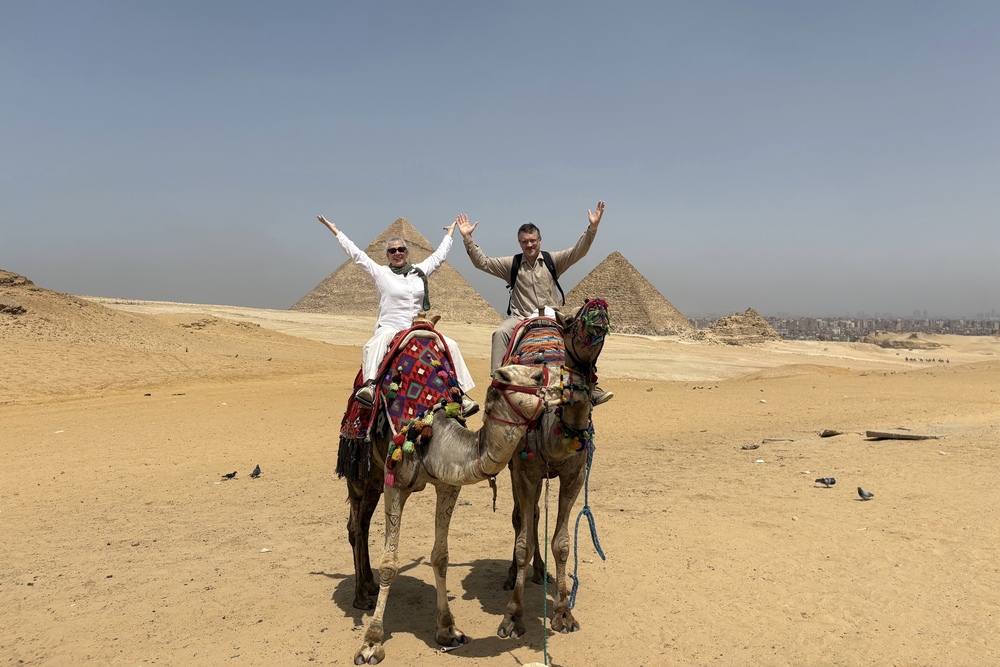 Tamara and Wolfgang Tsoutsouris on camels with Khufu and Khafre pyramids in the background.