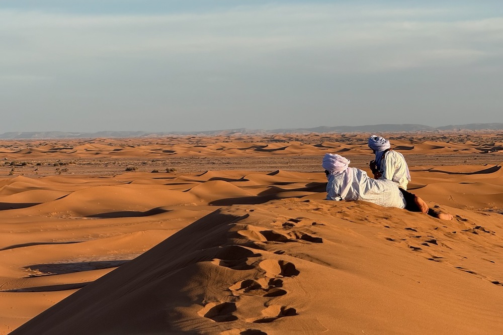 Bedouins sitting on sand dunes in the Sahara Desert, Morocco.