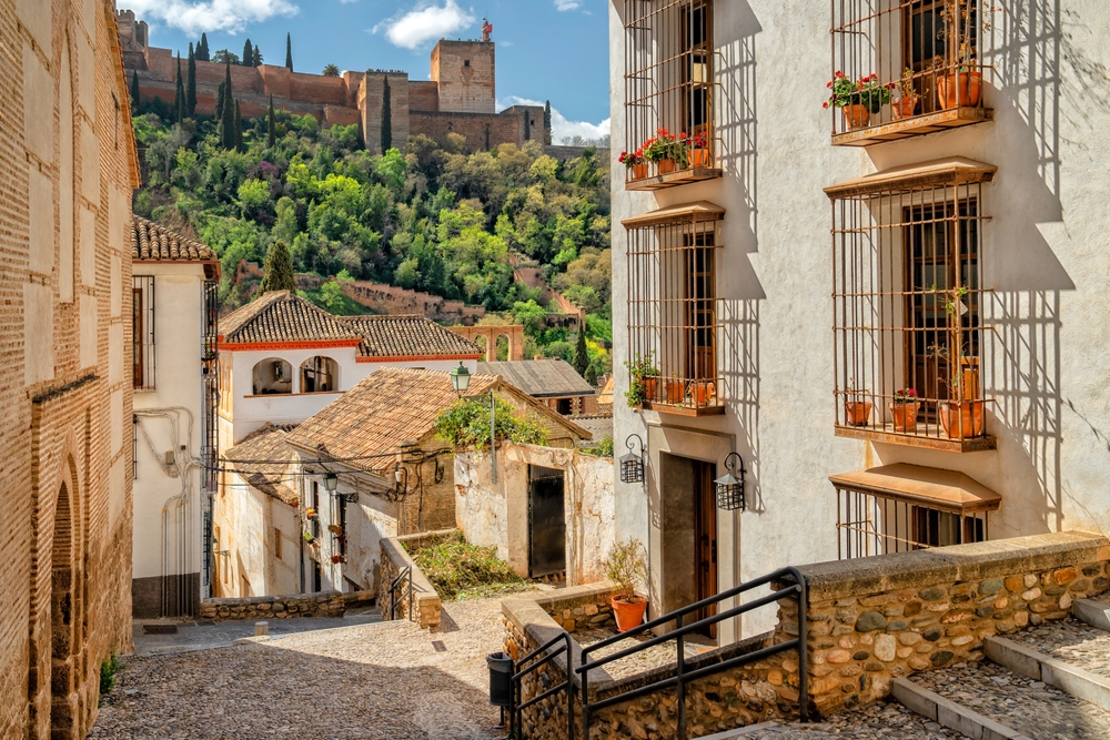 A historic old street made with cobblestone with a view of the Alhambra Palace in the background, Granada, Spain.