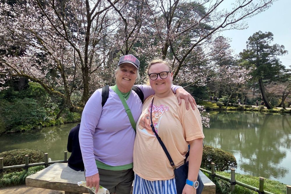 Travelers on a spring day surrounded by cherry blossoms in a garden with lake in Kyoto, Japan.