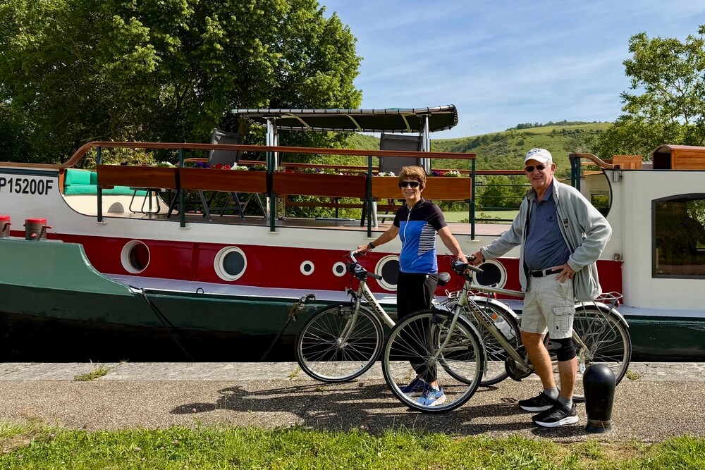 Joanne Dearth and Greg Bean standing with bicycles beside a canal boat in Burgundy, France.